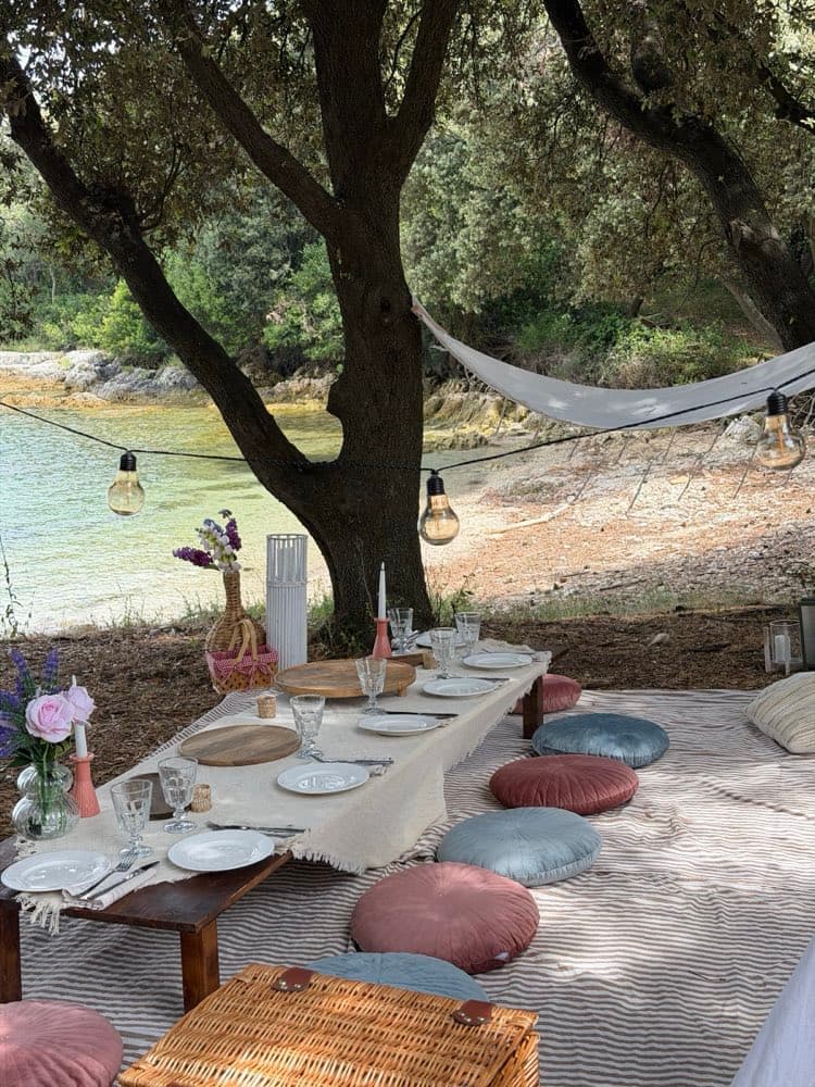 Long low table set for a group under a tree, with blue and pink cushions, hammock, string lights and a cove